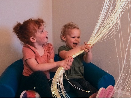 Two young children laughing as they hold a bundle of fibre optic sensory strands